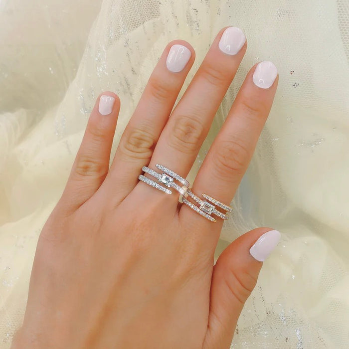 Hand wearing two diamond rings with light pink nail polish on a neutral background